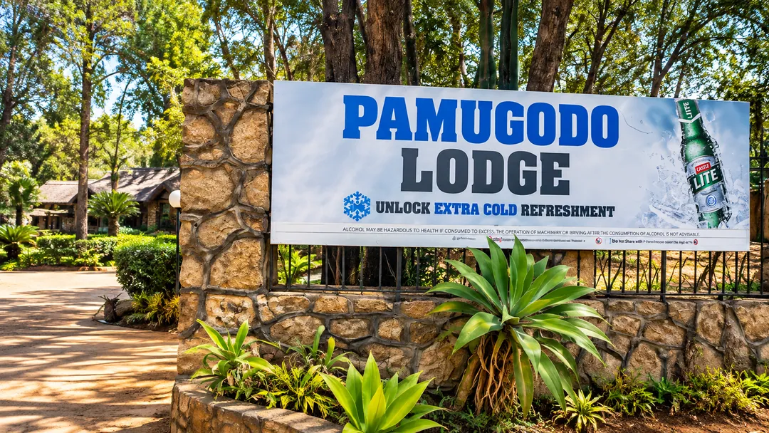 Stone entrance wall with a Pamugodo Lodge banner, surrounded by tropical planting