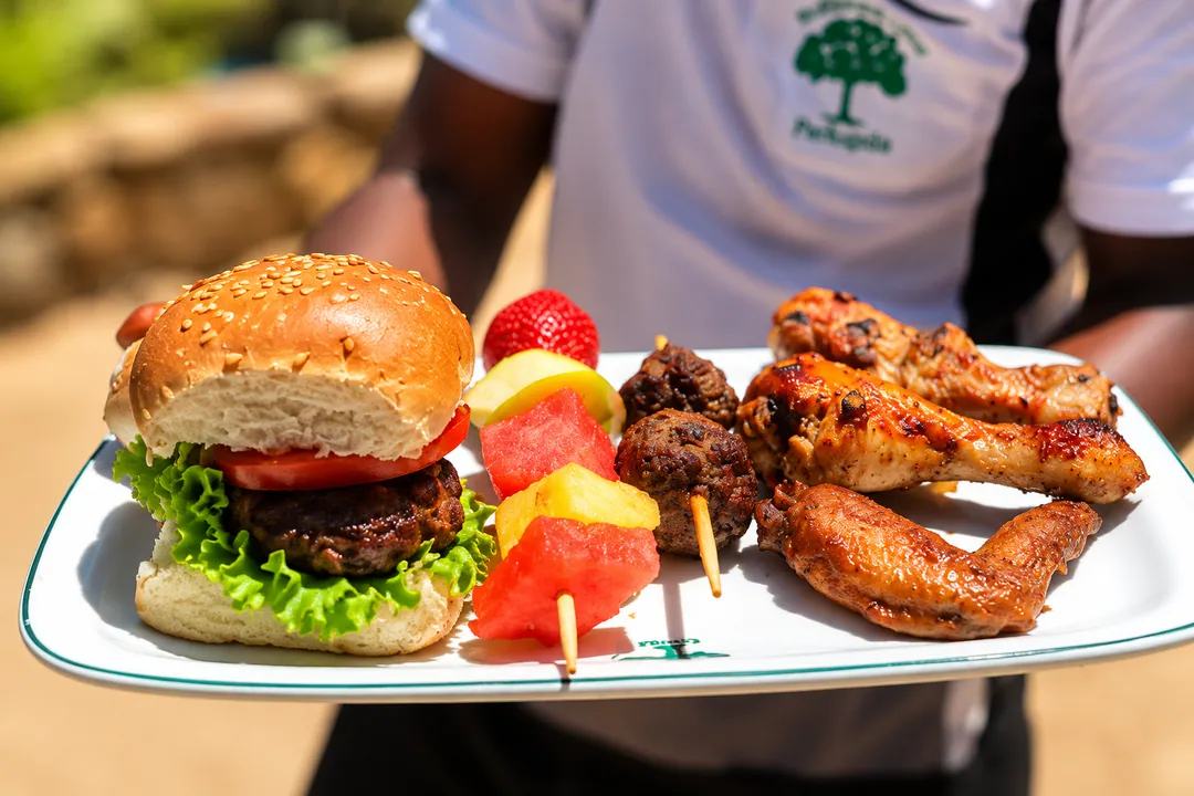 A server holding a platter with a burger, fresh fruit skewers and grilled chicken